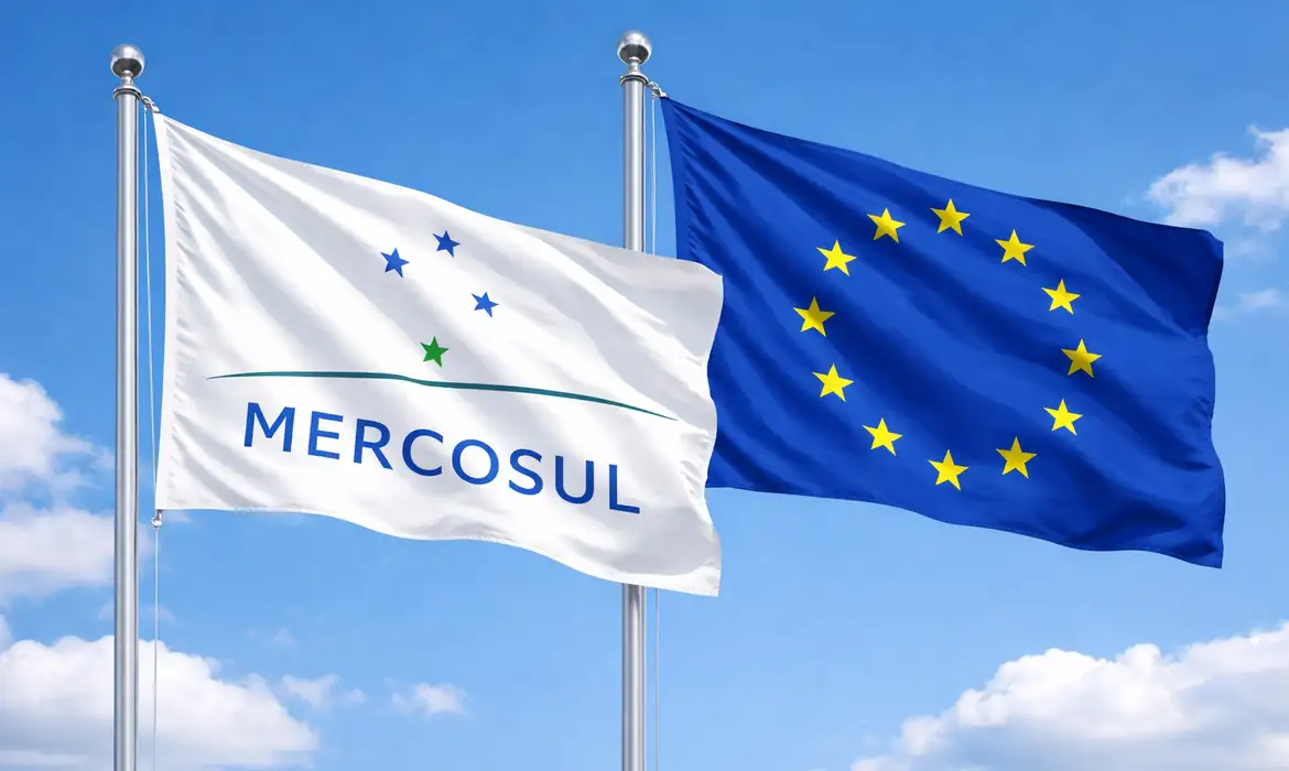 The Mercosul and European Union flags flying side by side on flagpoles against a blue sky