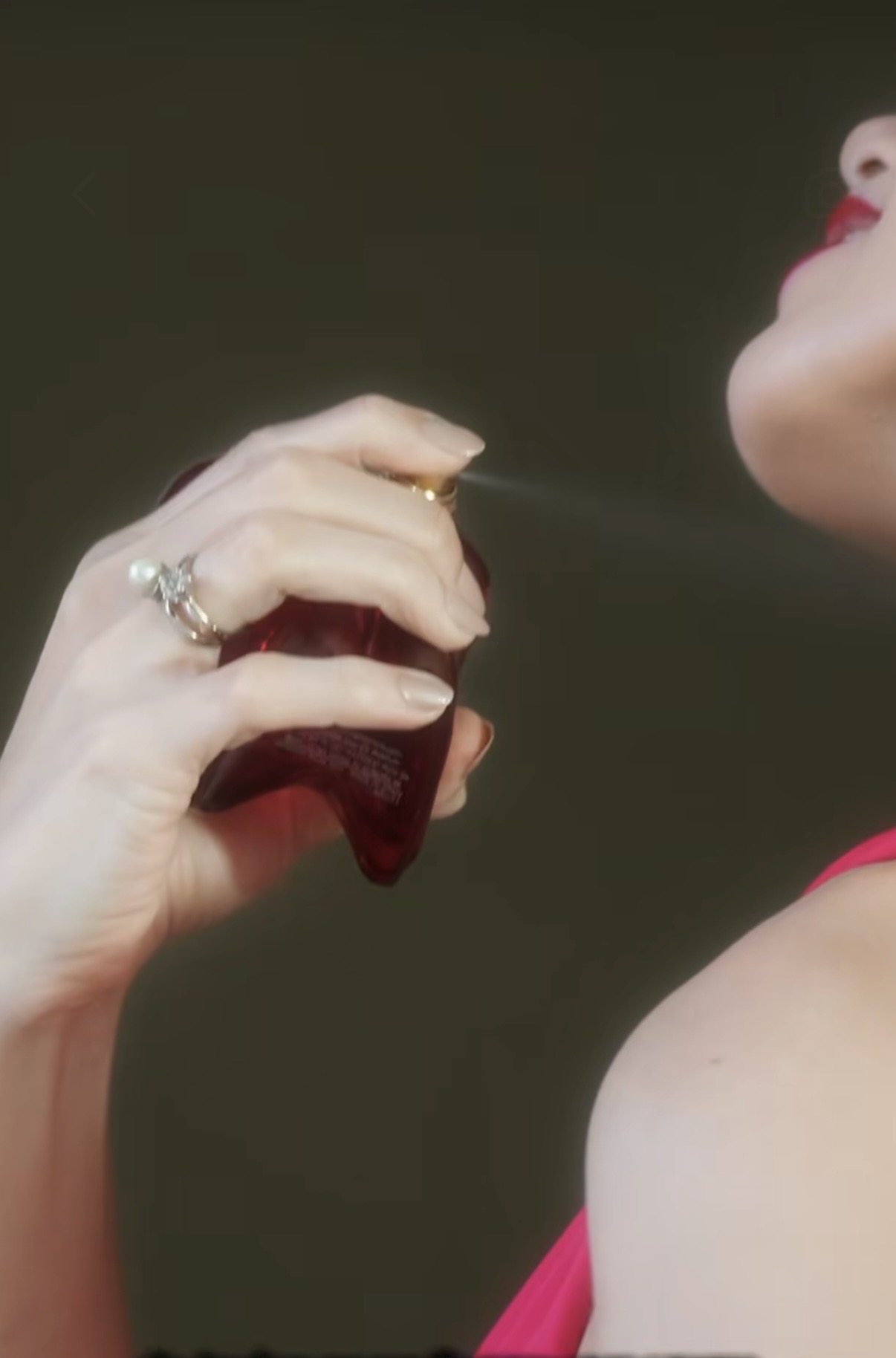 A woman in a pink top spraying a dark red perfume towards her face