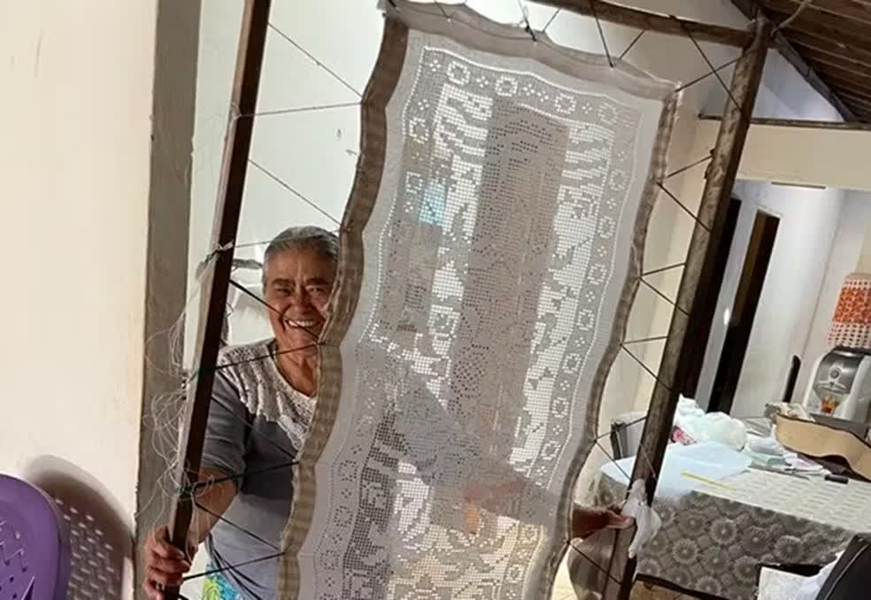 An embroiderer of the Reduto community holding a large Bordado Labirinto piece on a frame