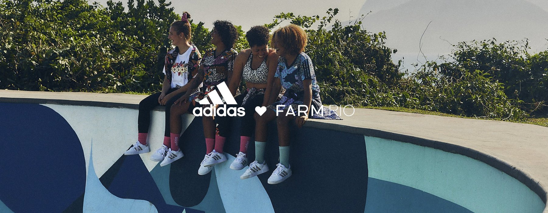 Four women in adidas x FARM Rio prints and white sneakers sitting on the edge of a painted skate bowl